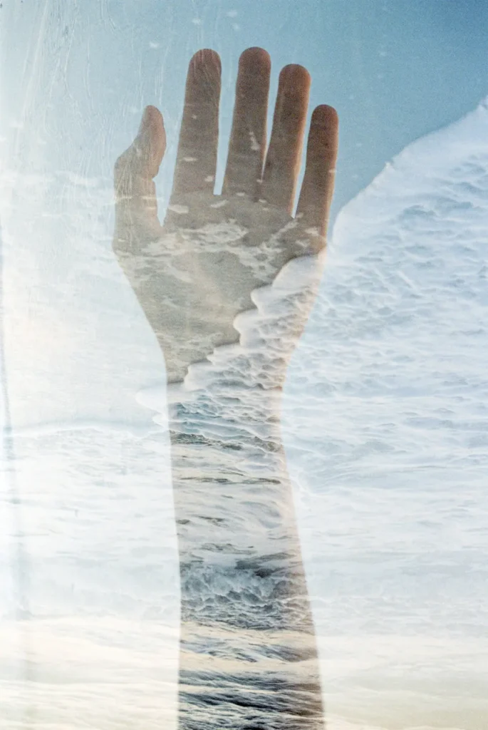 Fine art double exposure film photography of a hand overlaid with ocean waves by Jessica North.