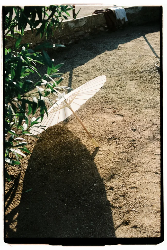 Minimalist analog film photography of a white paper parasol on sand with dramatic shadows, captured by Jessica North.