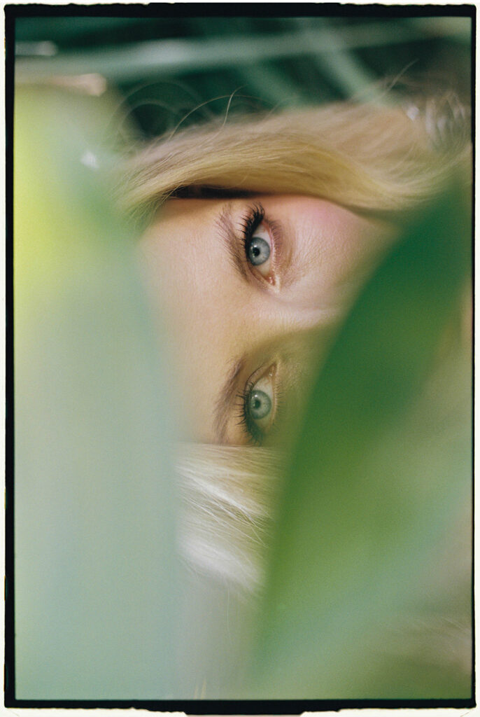 Mallorca Wedding Photographer Intimate analog film close-up of a bride's blue eyes peering through green leaves, with borders by Jessica North